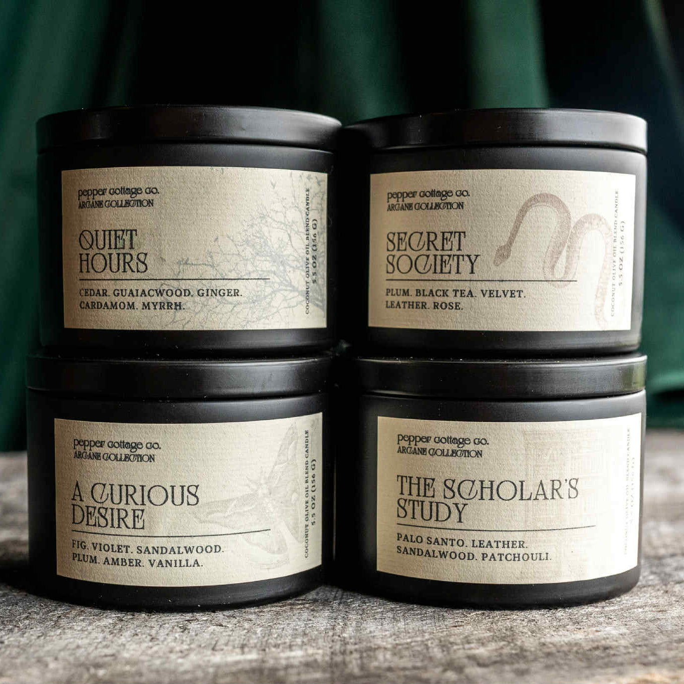 Four candles with labels on a wooden surface against a green curtain background