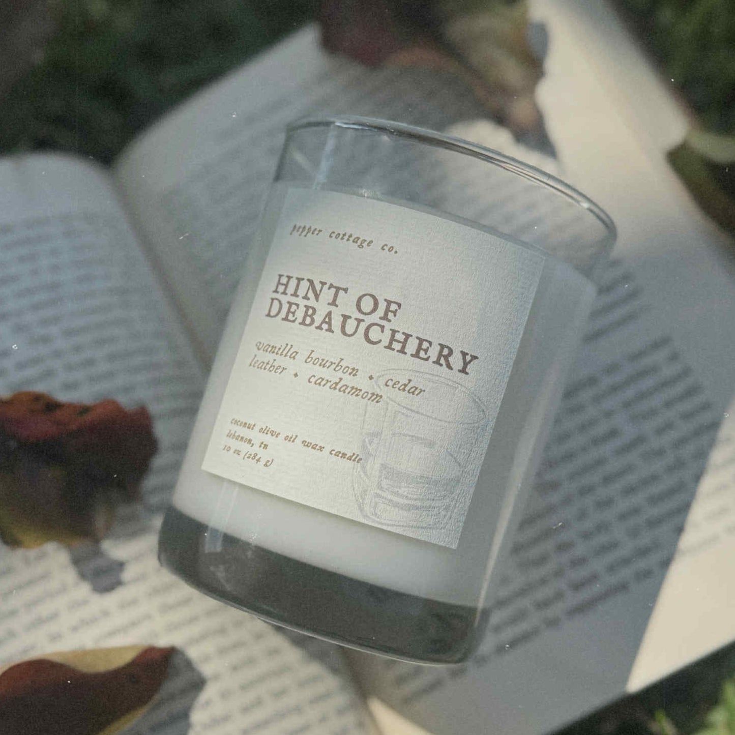 Candle labeled 'Hint of Debauchery' on an open book outdoors