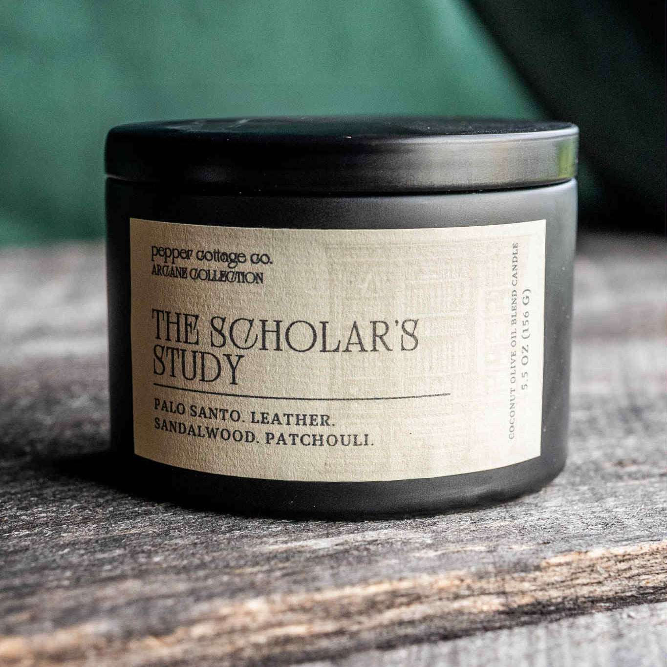 Candle labeled 'The Scholar's Study' on a wooden surface with a blurred green background