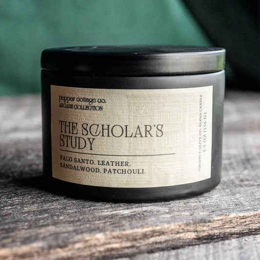 Candle labeled 'The Scholar's Study' on a wooden surface with a blurred green background