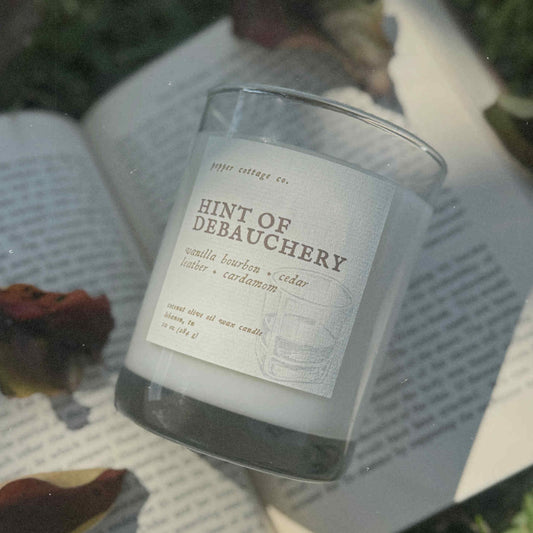 Candle labeled 'Hint of Debauchery' on an open book outdoors